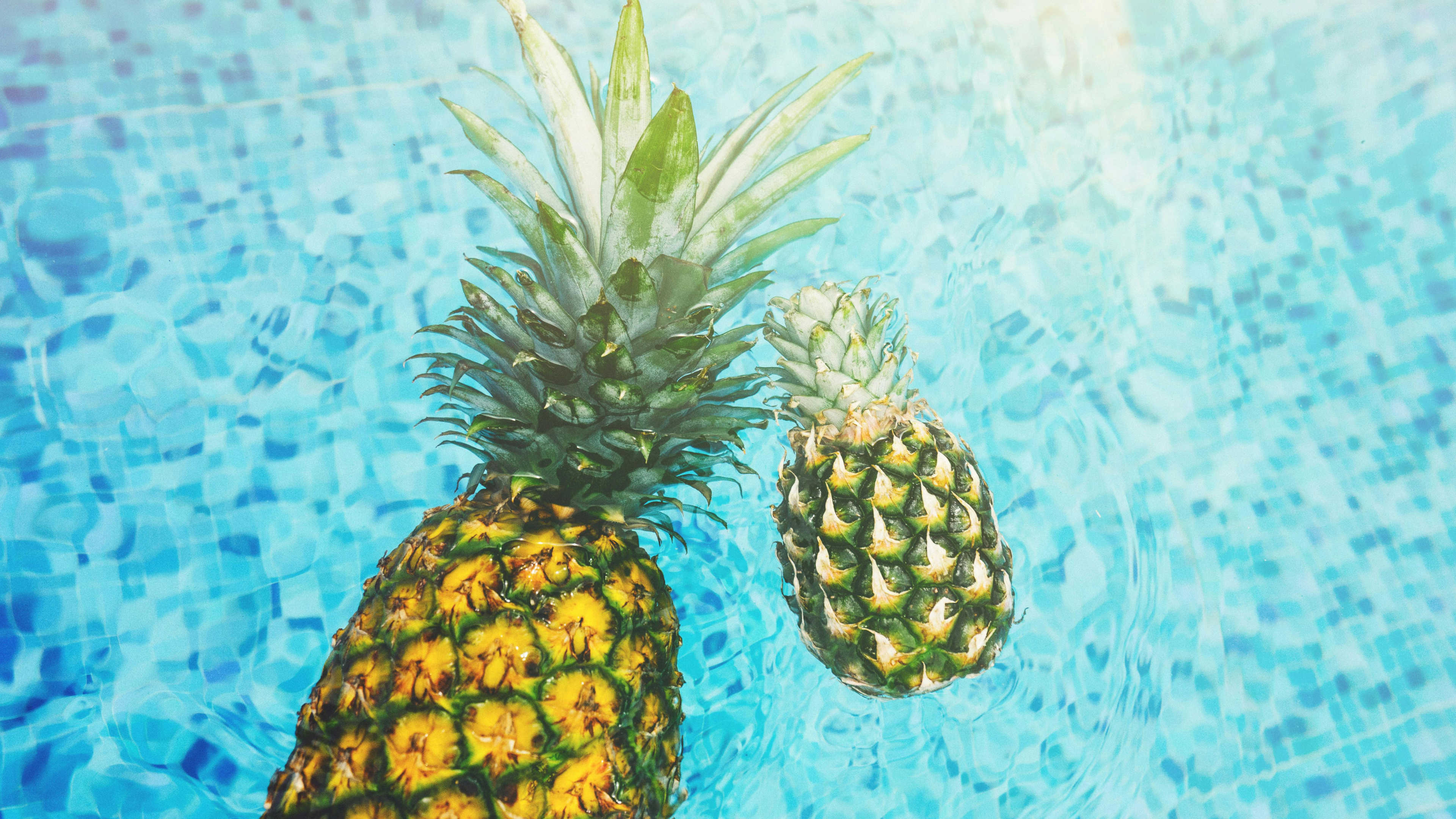 Two pineapples floating in a pool