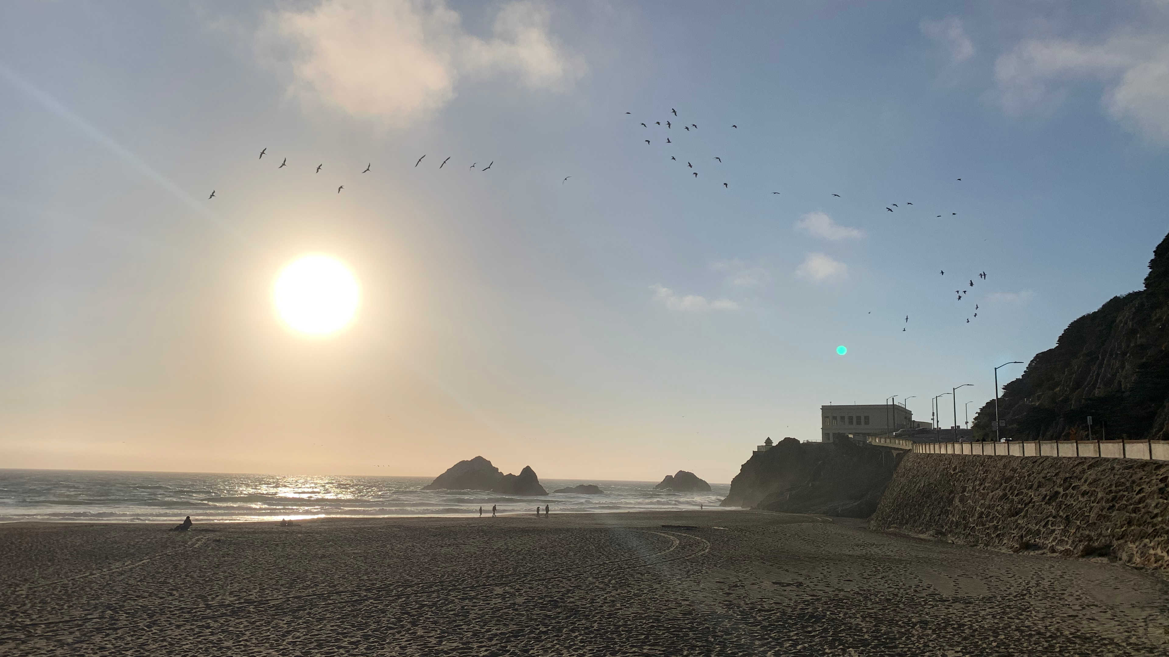 Bright sun setting over the Pacific Ocean, with the Cliff House overlooking the water